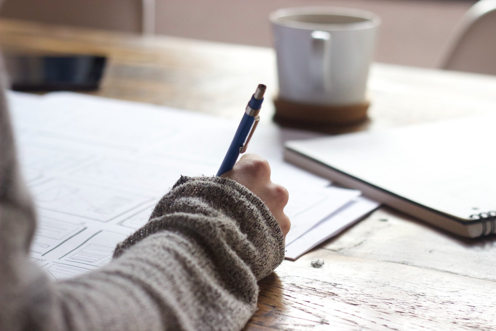 notes person writing on brown wooden table near white ceramic mug
