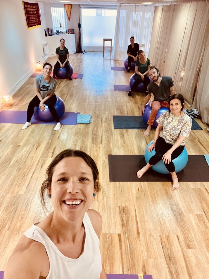 A cheerful woman in active wear exercises with a yoga ball indoors, promoting wellness.